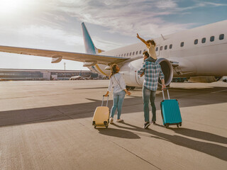A happy and cheerful family is at the bustling airport, excitedly approaching their airplane for...