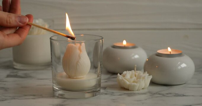 Woman lighting up beautiful flower shaped candle at white marble table, closeup