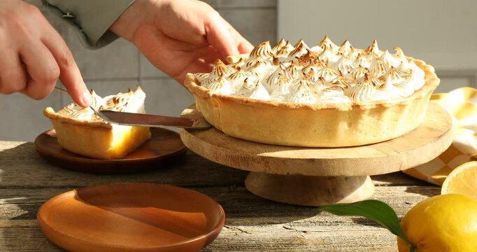 Woman serving piece of lemon meringue pie at wooden table, closeup