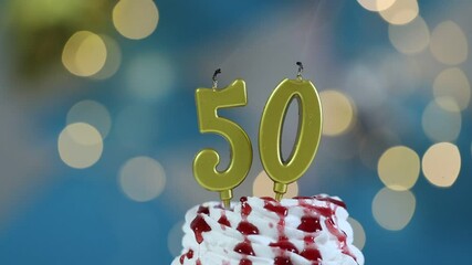50th birthday. Blowing out number shaped candles on cupcake against blurred background with lights, closeup. Bokeh effect