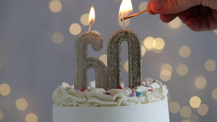 60th birthday. Woman lighting number shaped candles on cake against grey background with blurred lights, closeup. Bokeh effect