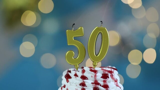 50th birthday. Blowing out number shaped candles on cupcake against blurred background with lights, closeup. Bokeh effect