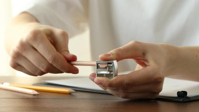 Woman sharpening graphite pencil and writing on paper sheet at wooden table, closeup