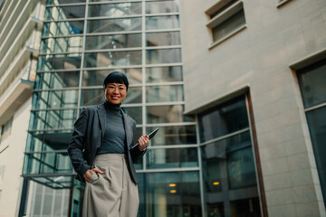 Smiling businesswoman holding tablet in front of modern office building