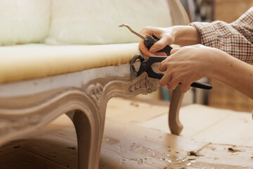 Hands removing staples from antique furniture during upholstery repair in workshop.