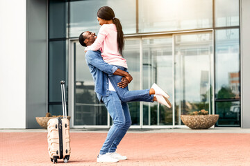 Long Awaited Reunion. Happy Excited African American Couple Meeting Near Airport Exit After Arrival, Overjoyed Black Man Lifting Wife In Air, Returning Home After Flights Resumption, Copy Space