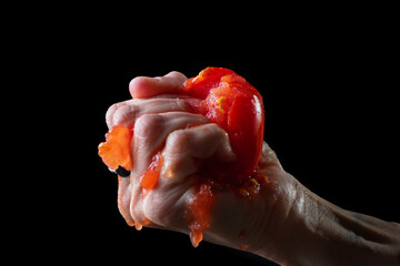 Hand squeezing a dripping tomato in front of a black background.