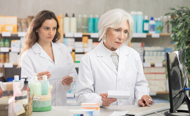Obraz premium Two female pharmacists employee using computer, remote document flow. Electronic database of drugs, international classification of diseases. Detailed list of drugs for treatment of colds