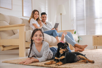 Little girl with puppy lying while parents sitting on sofa in living room