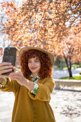 A young woman enthusiastically taking a cheerful selfie in a vibrant autumn park setting