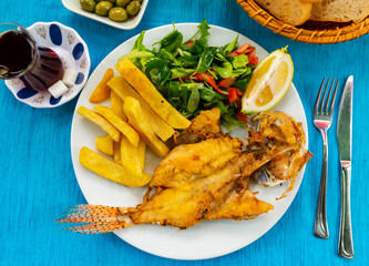 Roasted lionfish with fried potatoes and fresh greens, popular turkish dish