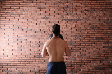 Athletic man doing exercise with medicine ball near red brick wall, back view