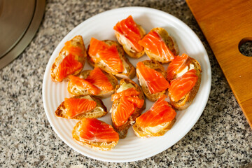 Closeup of appetizing canapes of baguette with butter and fillets of salted salmon served on white plate