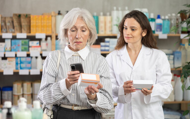 Senior woman scans barcode on a package of antibiotic pills with a mobile , she reads detailed instructions on the website and consults with a pharmacist