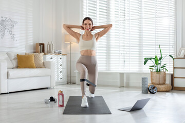 Obraz premium Happy woman exercising with elastic band near laptop at home