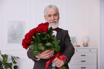 Senior man with bouquet of red roses at home