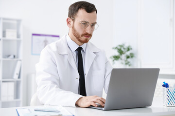 Fototapeta premium Professional doctor working on laptop at desk in hospital