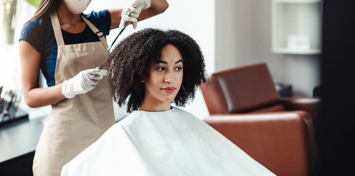 New beauty industry rules. Hairdresser in protective mask cutting hair of african american girl, free space