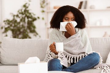 Fever, Cold, Flu Symptoms And Folk Medicine. Sick ill black woman covered in blanket blowing her...