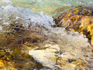 clear mountain river water flowing over colorful stones, creating a vibrant mix of golden reflections, bubbles, and fluid texture. dynamic