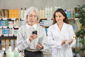 Mature woman scans a barcode on her smartphone camera and consults with a pharmacist about choosing an anti-aging cream with collagen. Process of buying and paying by QR code