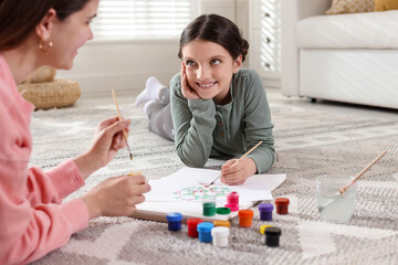 Girl and her mother drawing family tree with paints on floor indoors