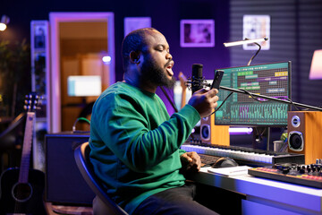 Skilled musician recording a new song written by him in home studio, reading lyrics from his phone...
