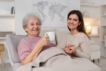 Obraz premium Grandmother with hot drink and her granddaughter at home. Elderly care