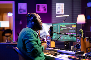 Male musician recording a new song on microphone in home studio, working on editing the recorded...