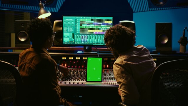 Team of producer and artist use tablet with mockup display in professional studio, mixing and mastering tracks after recording session. Experts working in control room with console. Camera B.