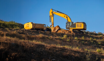 An excavator with a digging bucket digging dirt with a water truck spraying water © F Armstrong Photo