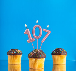 Birthday candle with the number 107 - Three cupcakes on a blue background