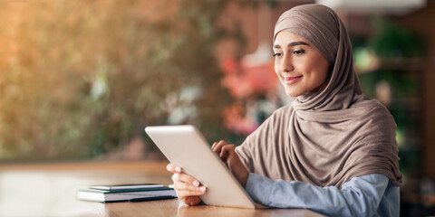 Beautiful young muslim woman in hijab blogger working at cafe, using digital tablet, copy space