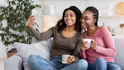 Happy black girls besties taking selfie together while drinking tea at home, copy space
