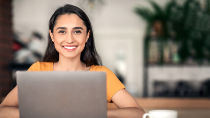 Pretty smiling arab girl using laptop at cafe, studying or working online, copy space