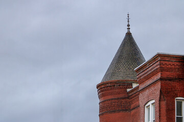 Historical brick tower with pointed roof against overcast sky in urban setting