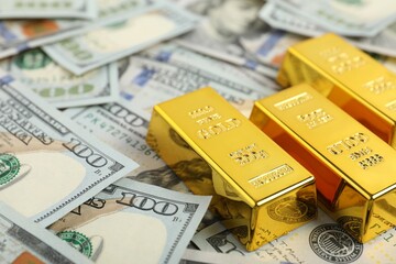 Shiny gold bars on dollar banknotes, closeup. Space for text