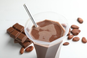 Tasty chocolate milk, bars and cocoa beans on white wooden table, closeup