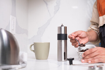 Man scooping coffee beans with spoon next to grinder and cup