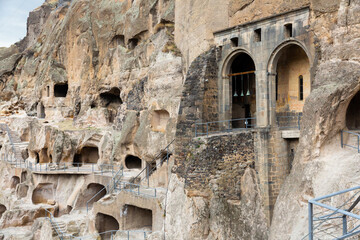 View of carved into rock caves of ancient monastic complex of Vardzia overlooking bells of temple of Assumption of Virgin in slopes of Erusheti Mountain near Georgian town of Aspindza in springtime