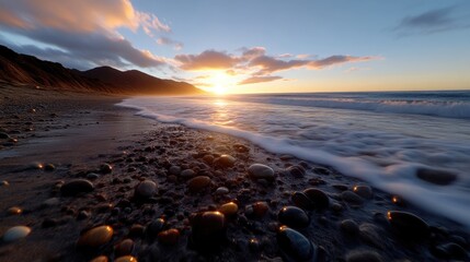 Obraz premium Golden sunset over a tranquil beach, with waves gently lapping onto the shore. Pebbles and rocks of various colors are scattered on the wet sand