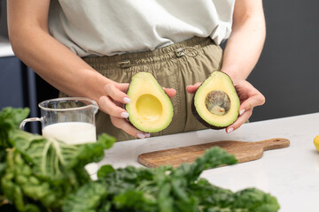 A woman holds two halves of a ripe avocado. Fresh avocado slices with ingredients for a healthy breakfast preparation