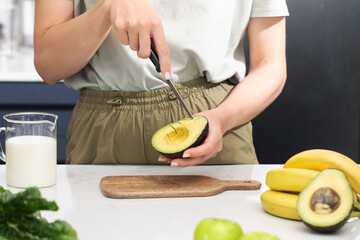 A woman cuts a ripe avocado. Healthy breakfast preparation with fresh fruits and avocado slices