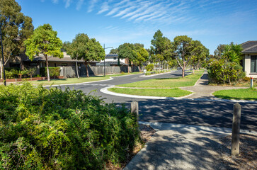 A suburban street view with a road and footpaths in a residential neighborhood. Mature trees line the streets, creating a comfortable community atmosphere. Williams Landing, Melbourne, Australia