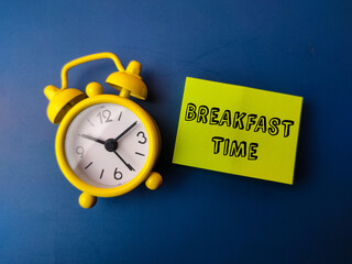 Alarm clock and sticky note with the word BREAKFAST TIME on blue background