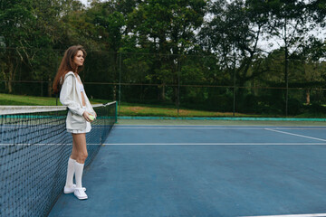 Obraz premium Young female tennis player in casual sportswear poses on court, showcasing confidence and athleticism, surrounded by a vibrant green background
