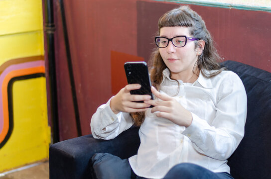 Young woman sit on couch, attentively looking at mobile phone screen with thoughtful expression, watching educational or informative content, following tutorial, attending webinar, or reading article