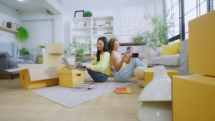 Happy two Asian women friend picking up things out to a paper box while preparing to move in of the new home. Relocation concept
