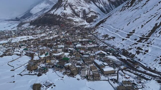 Aerial drone shot capturing the peaceful, snow-laden streets of Kaza in the middle of Spiti&rsquo;s rugged terrain, with only a few vehicles and footprints visible in the untouched snow.