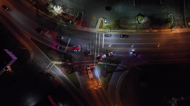 Car crash on american junction at night. Fire Truck, Police Car and Ambulance on street. American suburb district in America. Aerial top down. Traffic scene on freeway. Flashing lights of police.